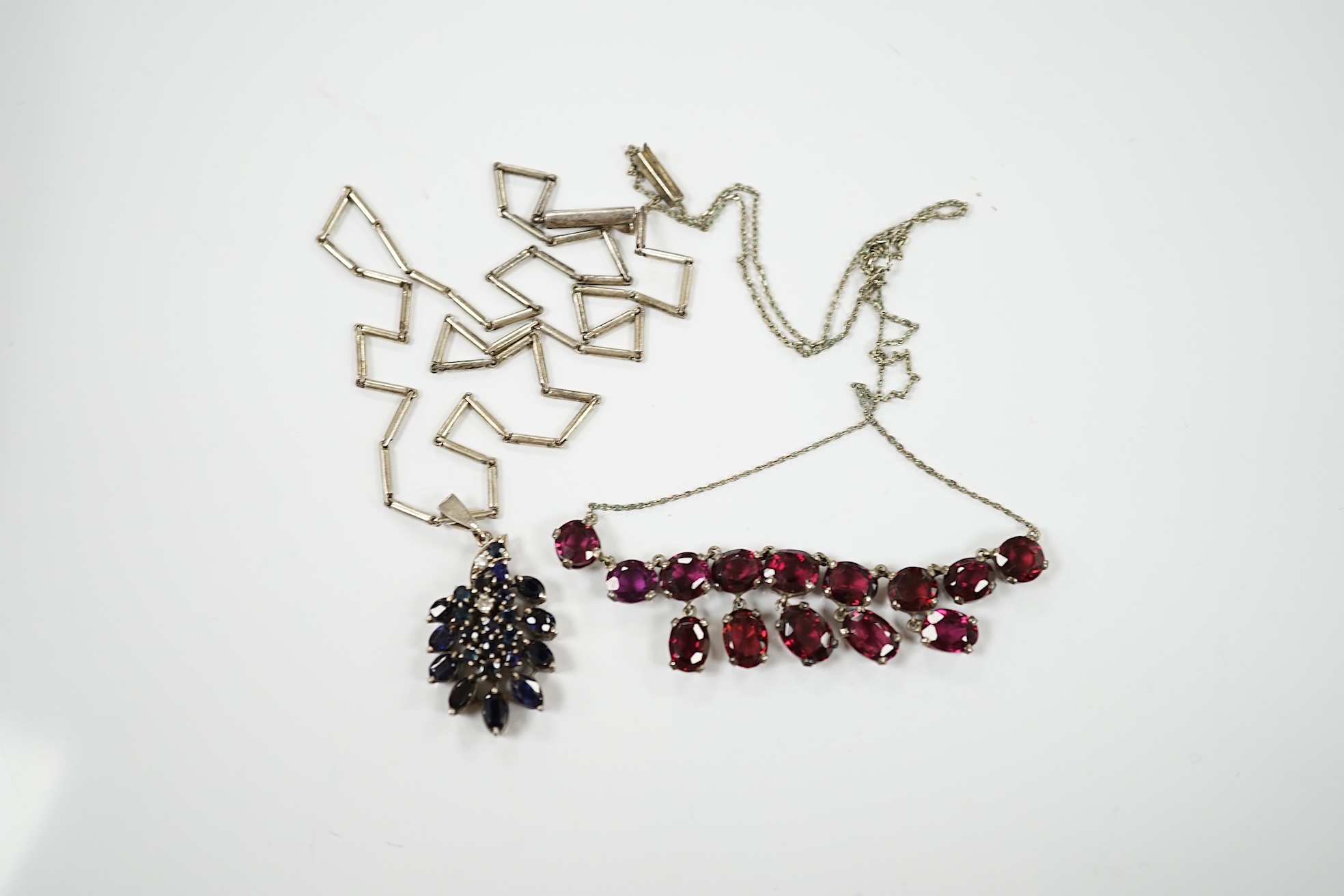 A white metal and garnet cluster set drop necklace, overall 48cm, together with a white metal, sapphire? and diamond cluster set pendant, on a white metal chain. Condition - fair